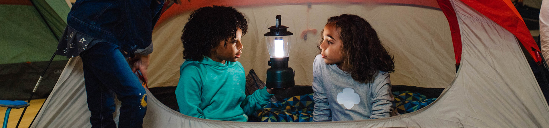  Two daisy kindergarten Girl Scouts holding lantern in tent camping wearing trefoil shirt. 